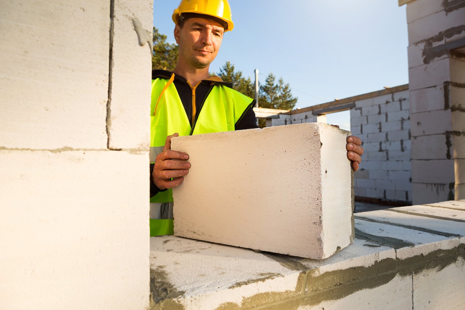 The builder holds a block of cellular concrete in his hands - the masonry of the walls