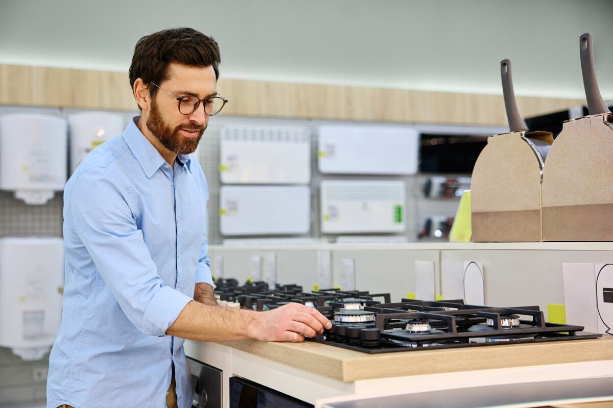 A Man Conducting a Thorough Inspection of a Gas Stove at a Modern Kitchen Appliance Store