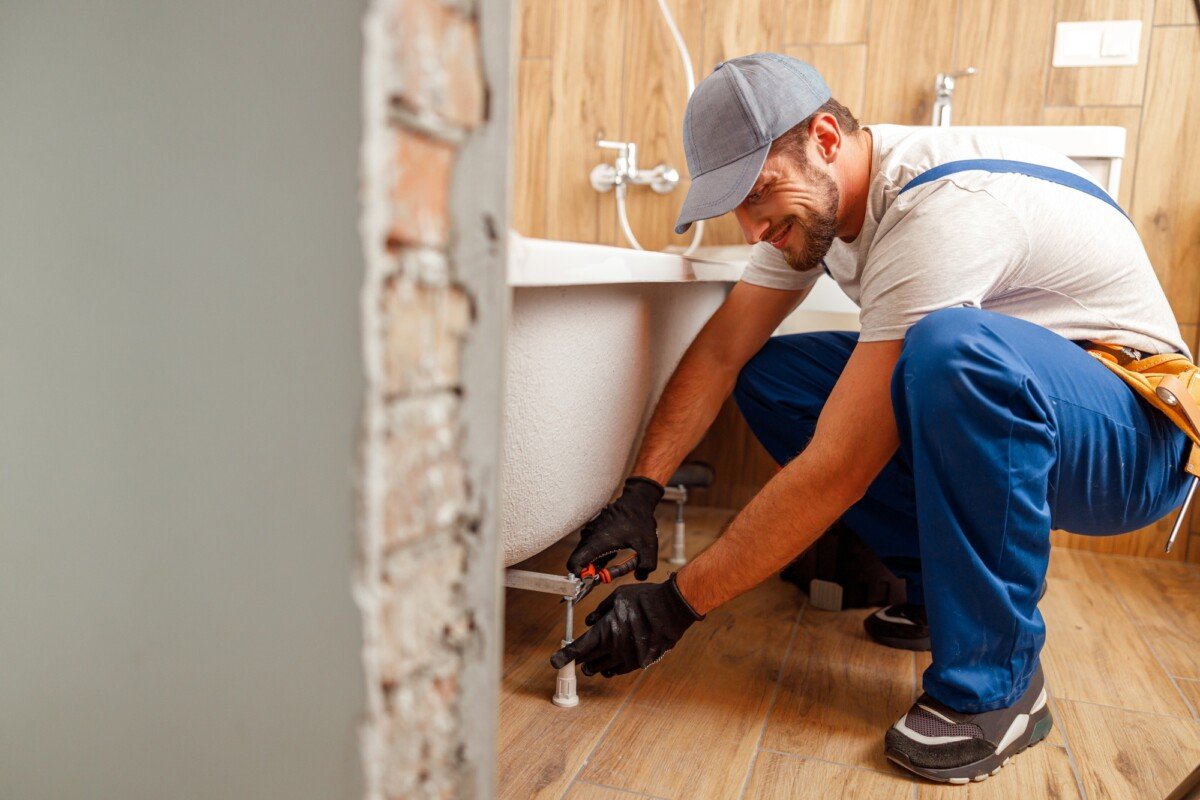 Cheerful plumber or technician preparing details for bathtub installation in bathroom