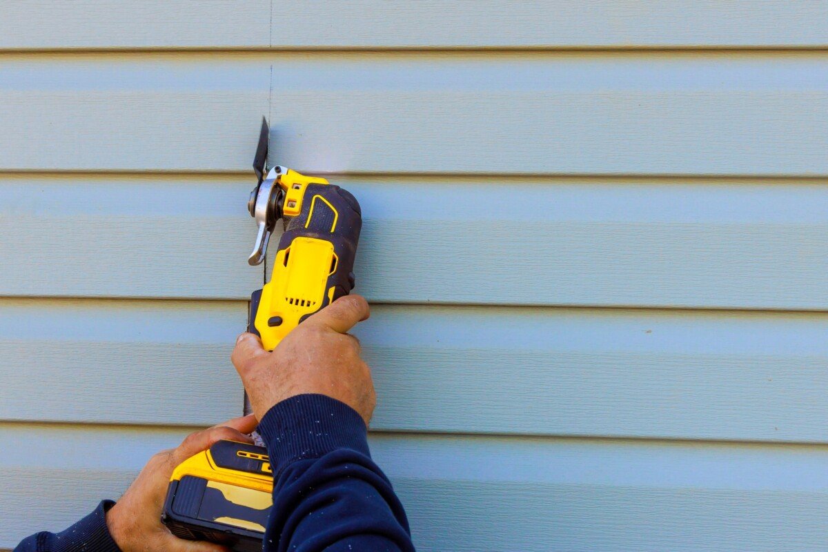 Damaged vinyl siding is removed using multi tool during reconstruction of a house