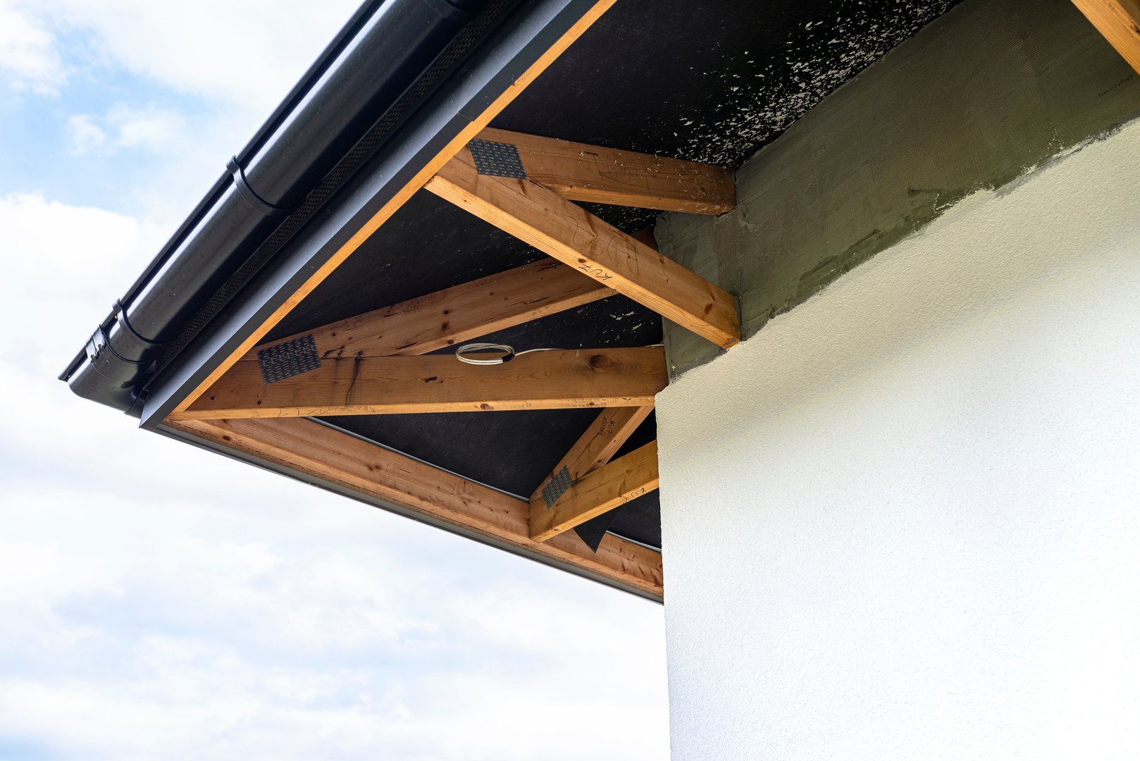 A newly applied layer of white silicone plaster on the wall of the house, visible roof trusses and a