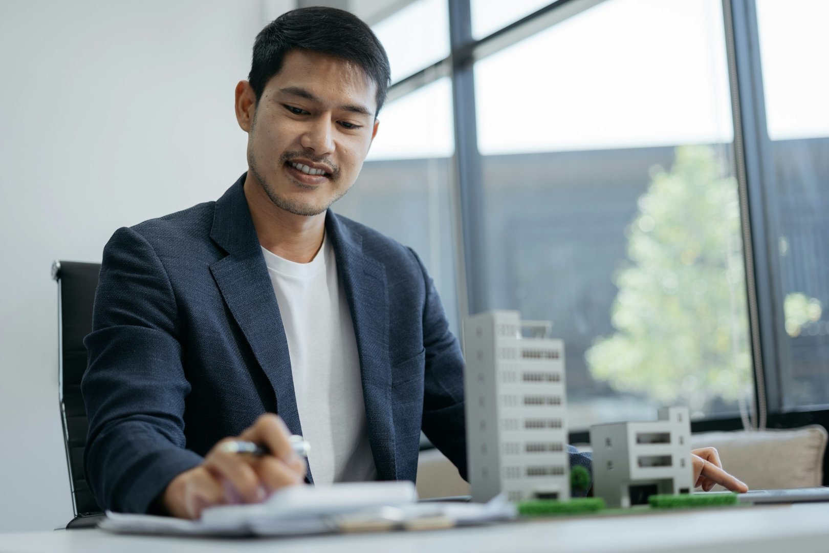 Home loan officer uses a calculator with a house plan on a wooden table.