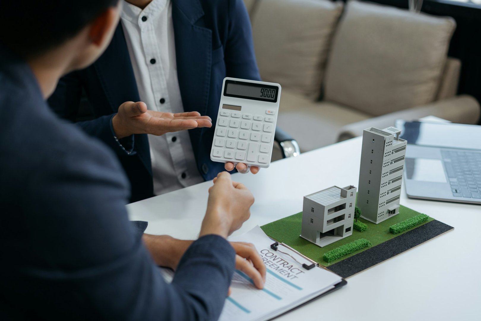 Home loan officer uses a calculator with a house plan on a wooden table.