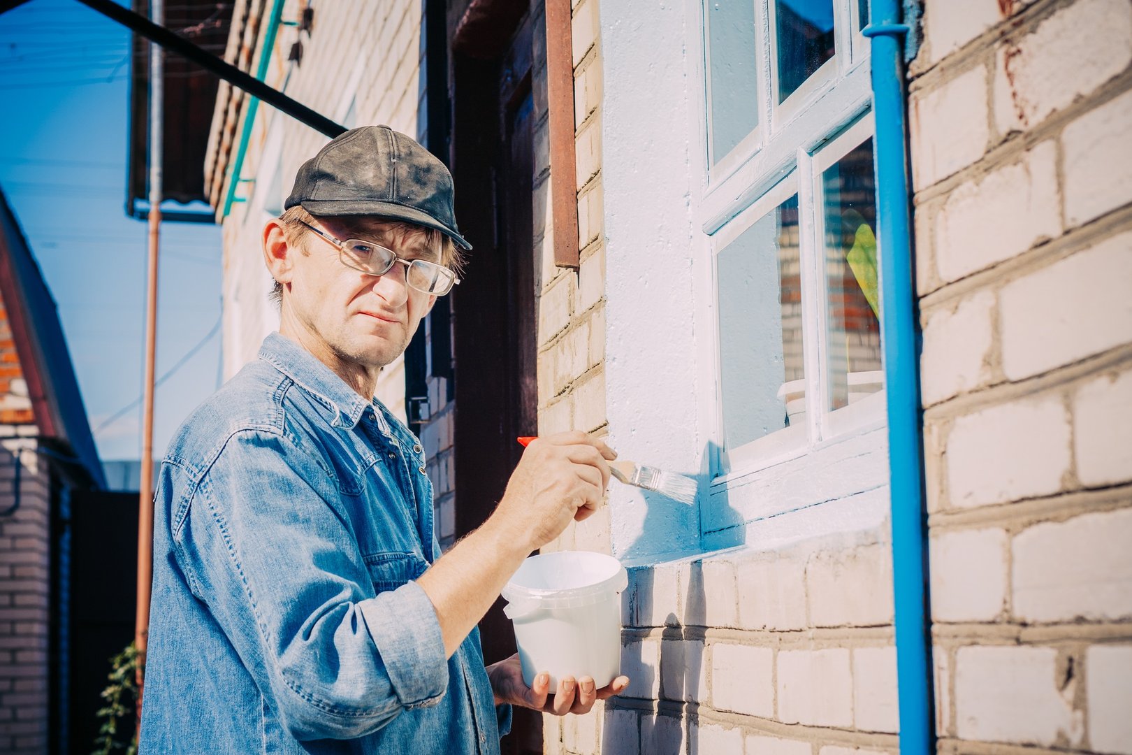 Mature Man In Glasses, Painting Window Frame Outside Of Private