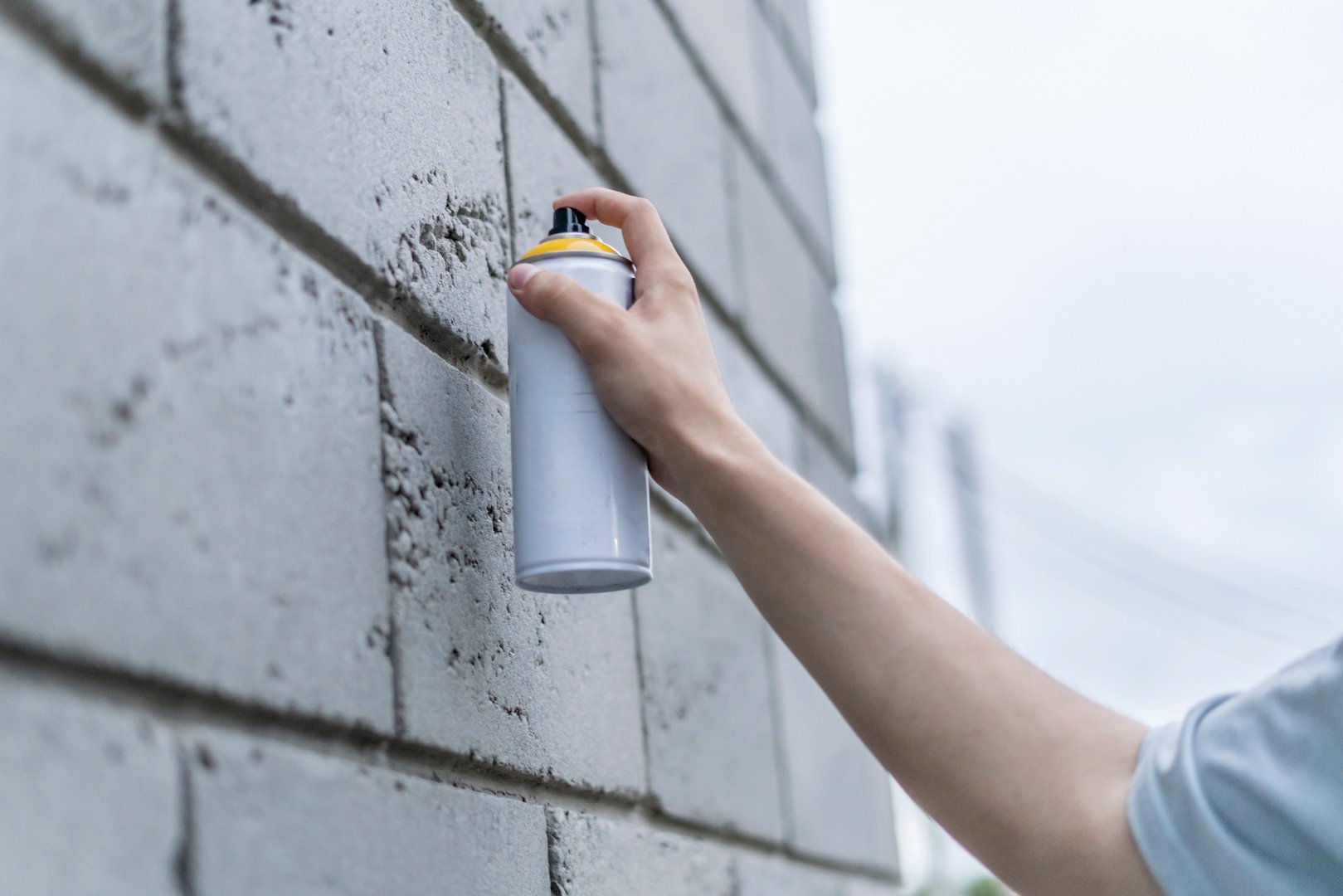 breaking the law: a man with a spray paint can painting a wall outdoor, damaging the building