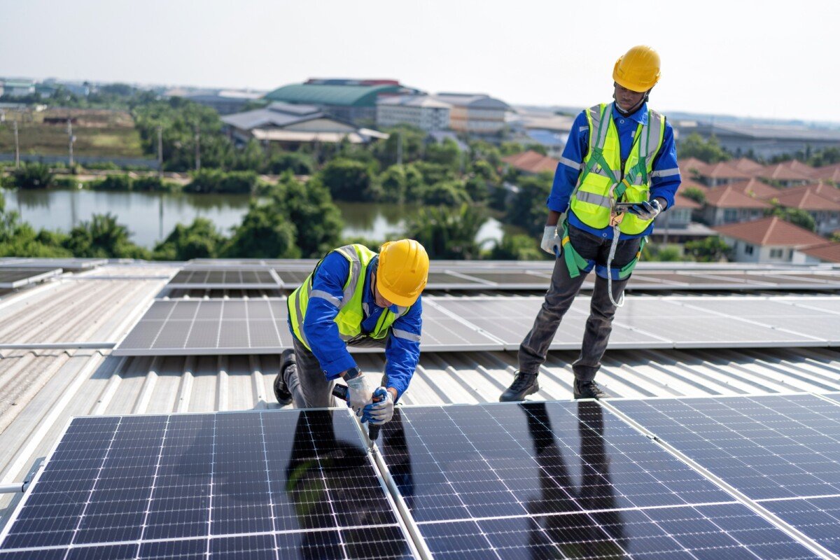 Engineer on rooftop kneeling next to solar panels photo voltaic with tool in hand for installation