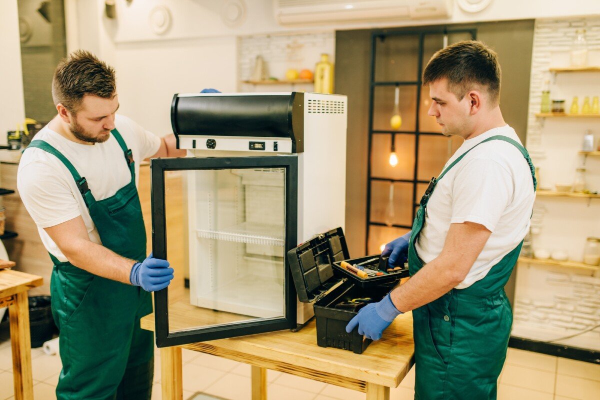 Two workers in uniform repair refrigerator at home