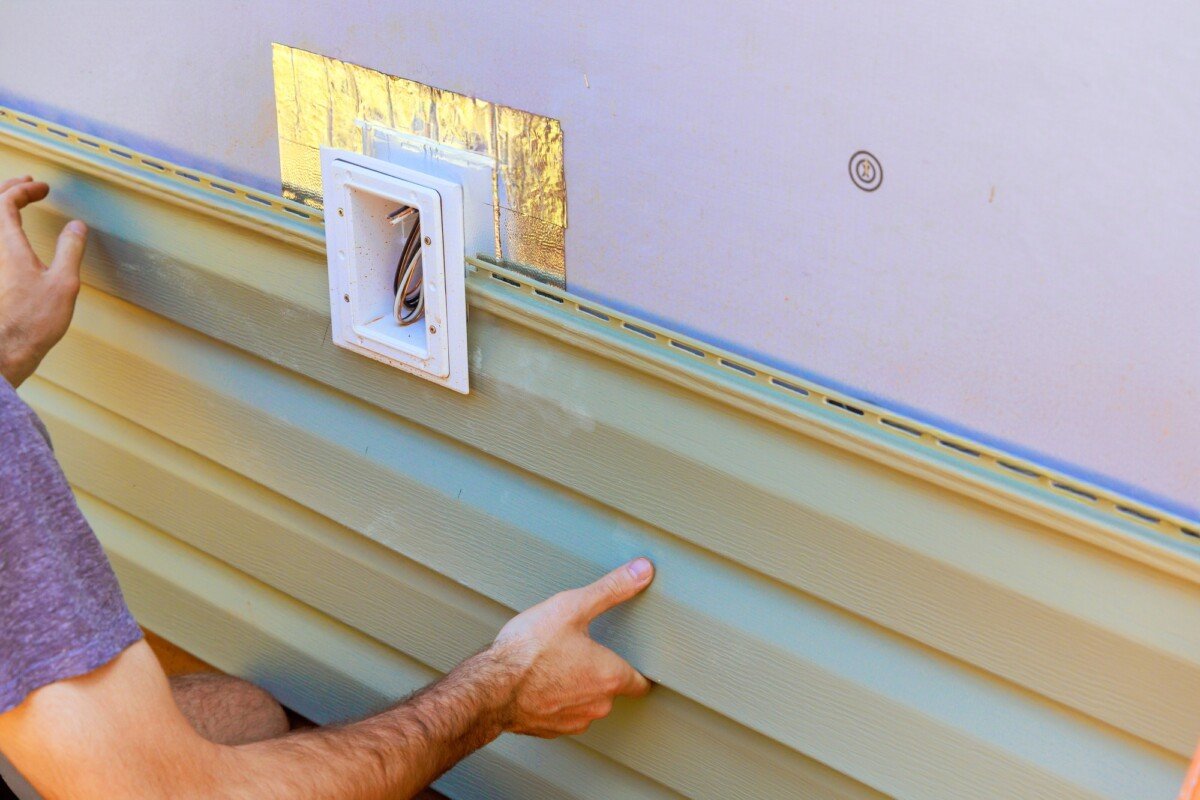 Vinyl plastic siding panels are installed on wall facade of a new building by an employee