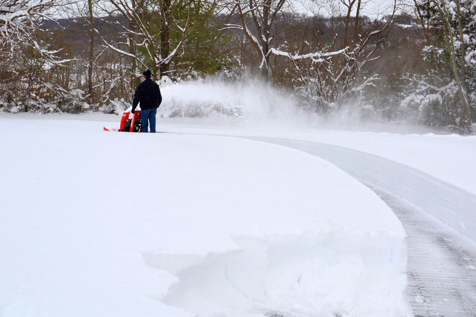 Man using a snow blower to clear his driveway in the winter