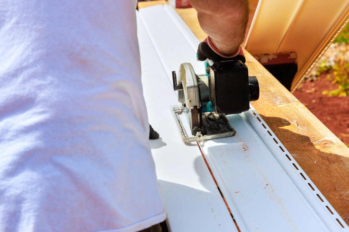 Workers cut plastic vinyl siding to a required size before installing it