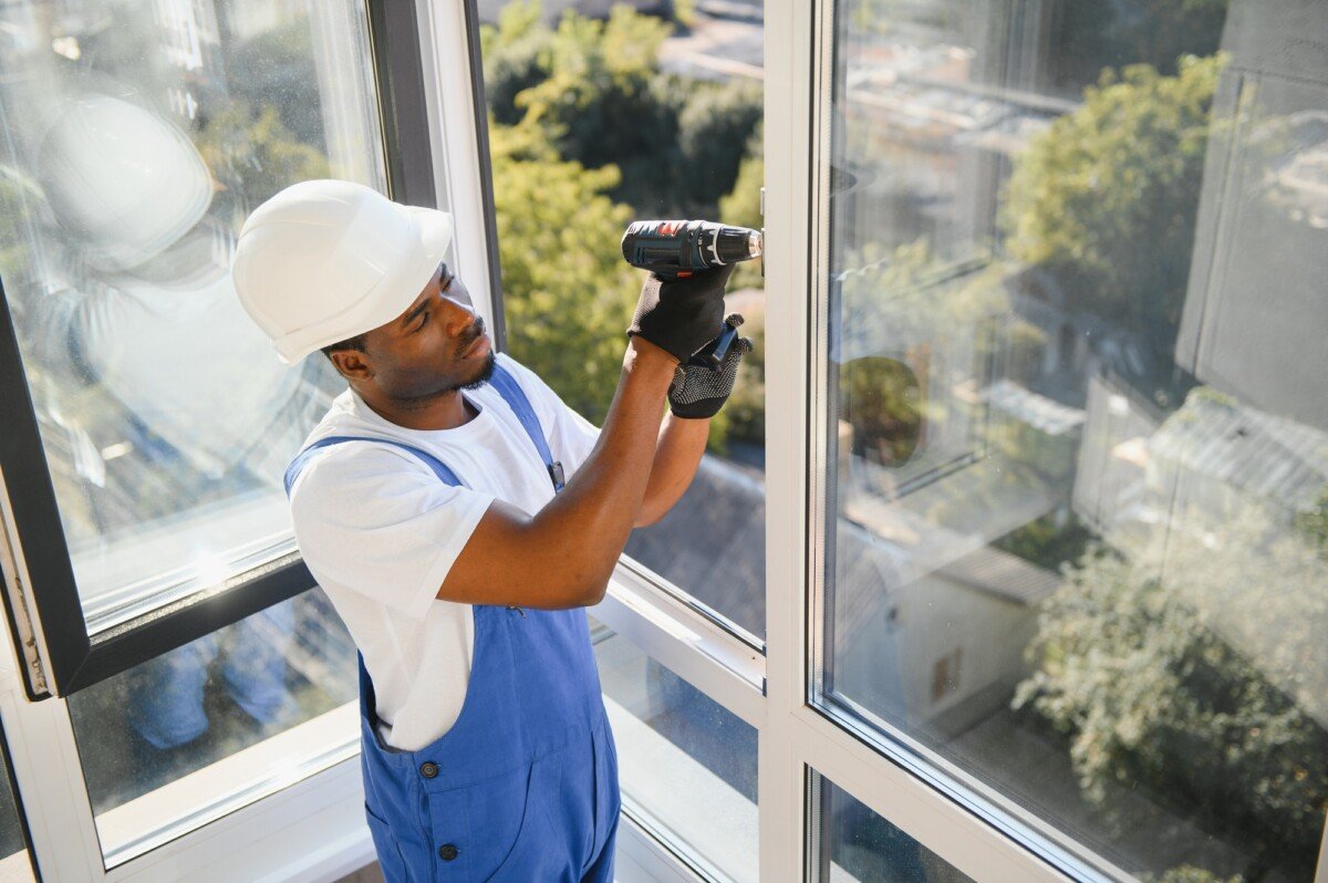 African Workman in overalls installing or adjusting plastic windows in the living room at home