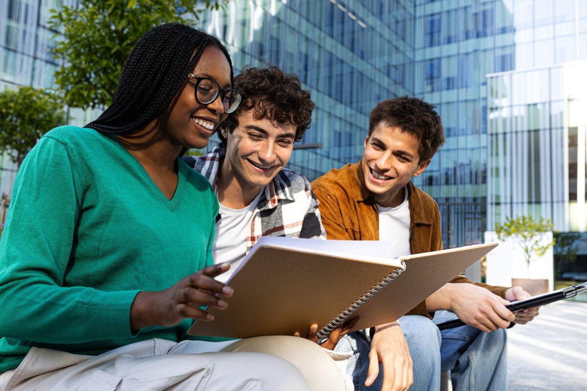 Multiracial college students studying together sitting on campus bench. Higher education concept.