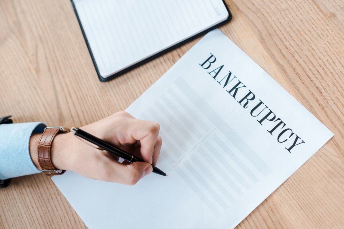 top view of man holding pen near paper with bankruptcy letters and notebook
