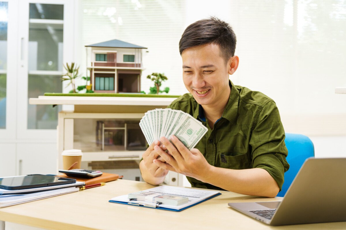 Asian businessman works alone at desk with a laptop, paperwork, and house model, on mortgages.