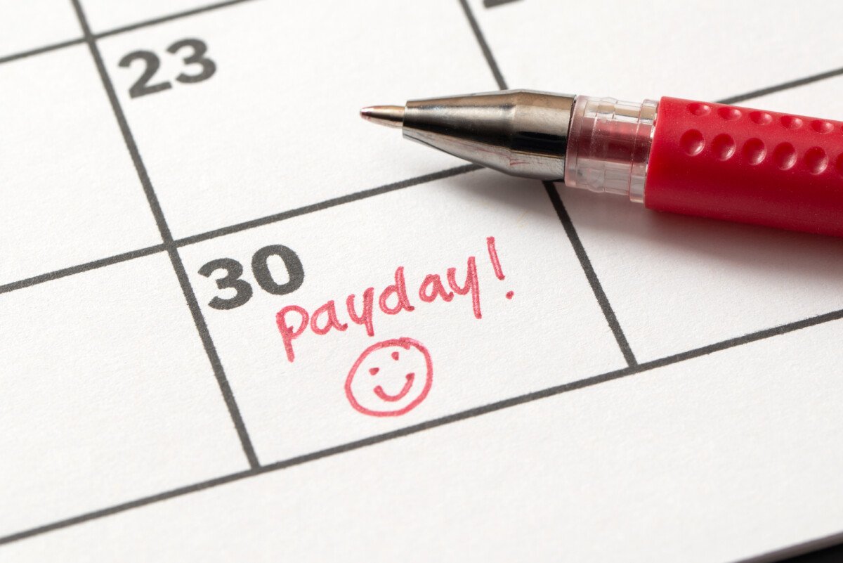 Payday reminder written on calendar with smiley face in red marker