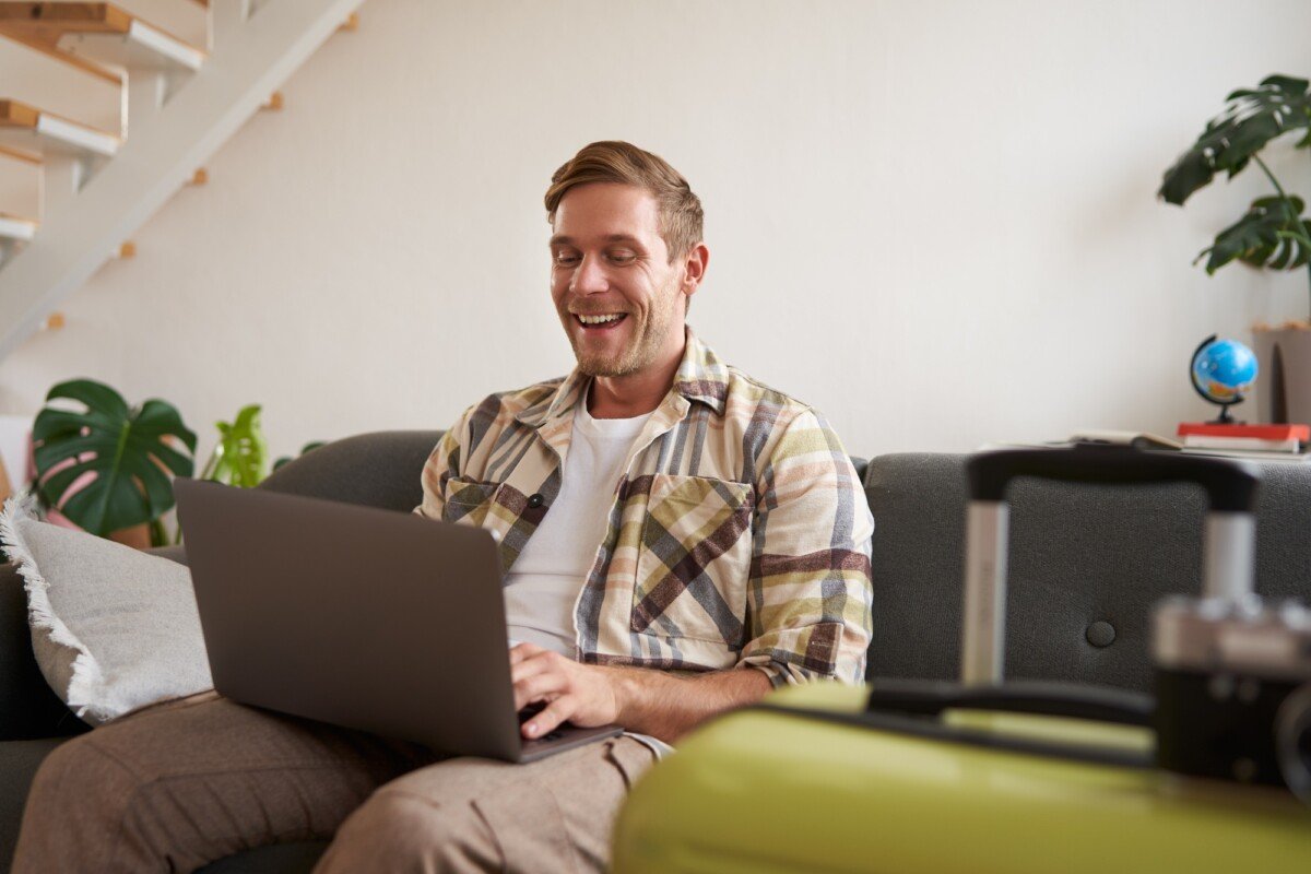 Portrait of happy young man, tourist booking his holiday with travel agency, looking at laptop