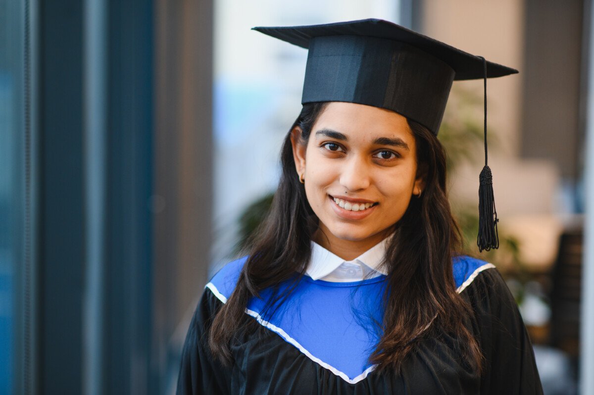 Young indian woman wearing graduation cap and gown, smiling at the camera, celebrating her educational achievement and future
