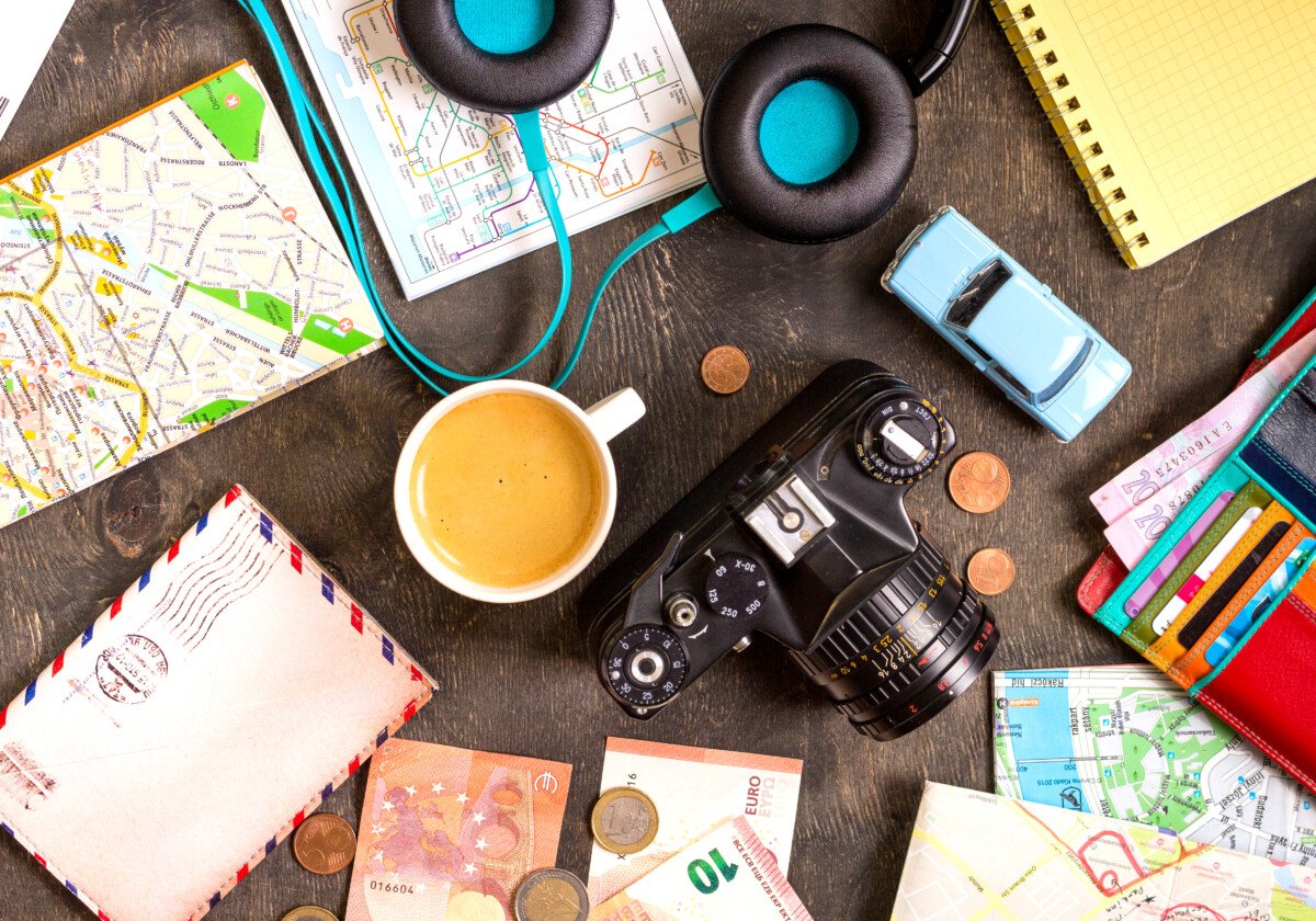 Camera, touristic maps, passport, toy car, coffee, headphones, wallet with credit cards, euro banknotes and coins on a…