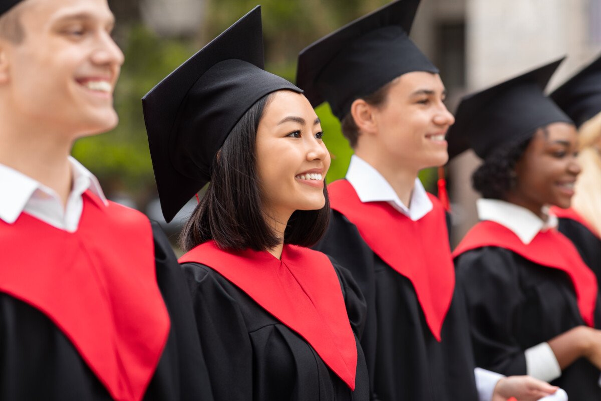Multiracial group of cheerfully graduates having graduation ceremony, wearing black and red graduation robes and caps,…