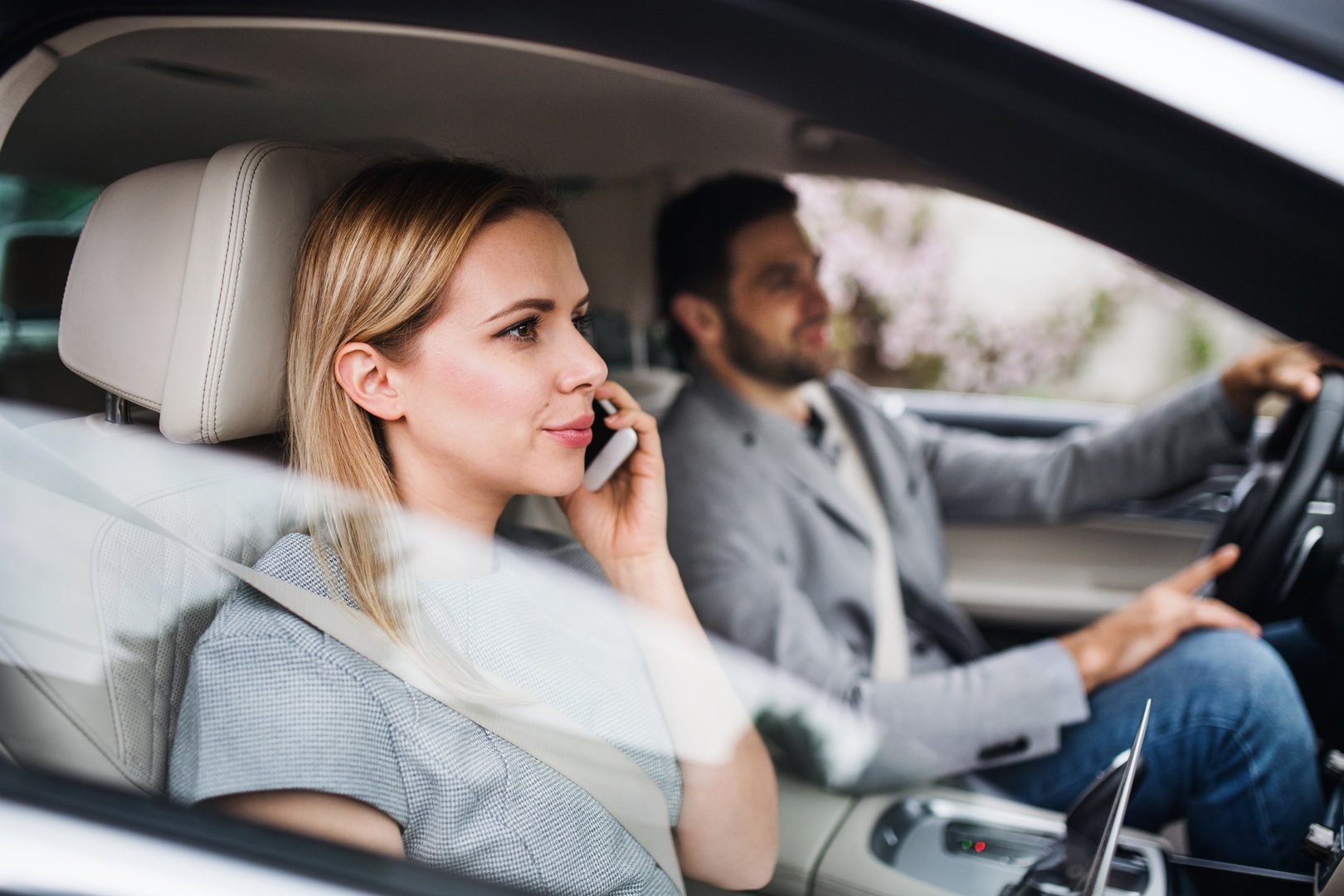 Happy young couple sitting in car, making phone call