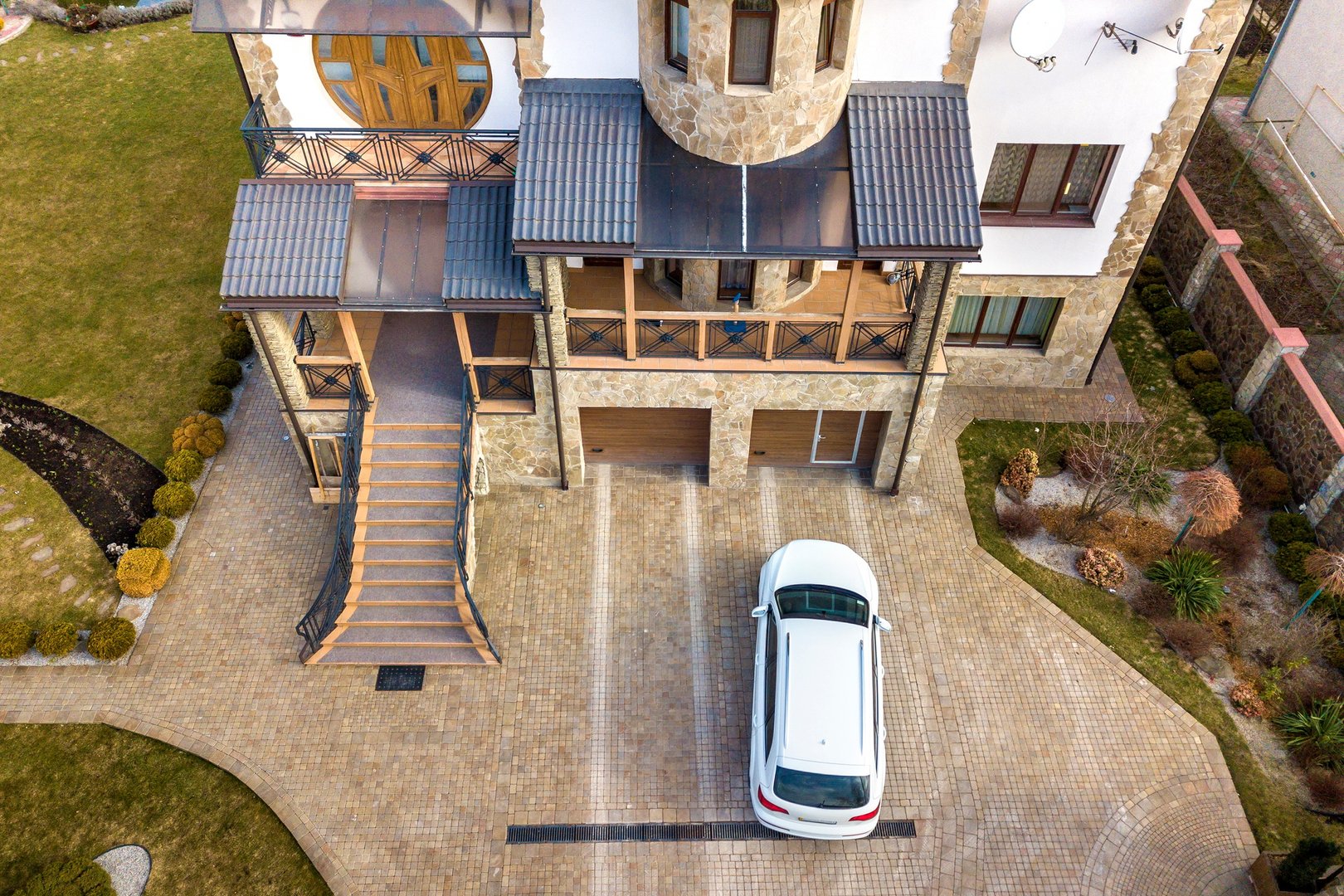 New white car parked in paved driveway with green lawn, decorative bushes