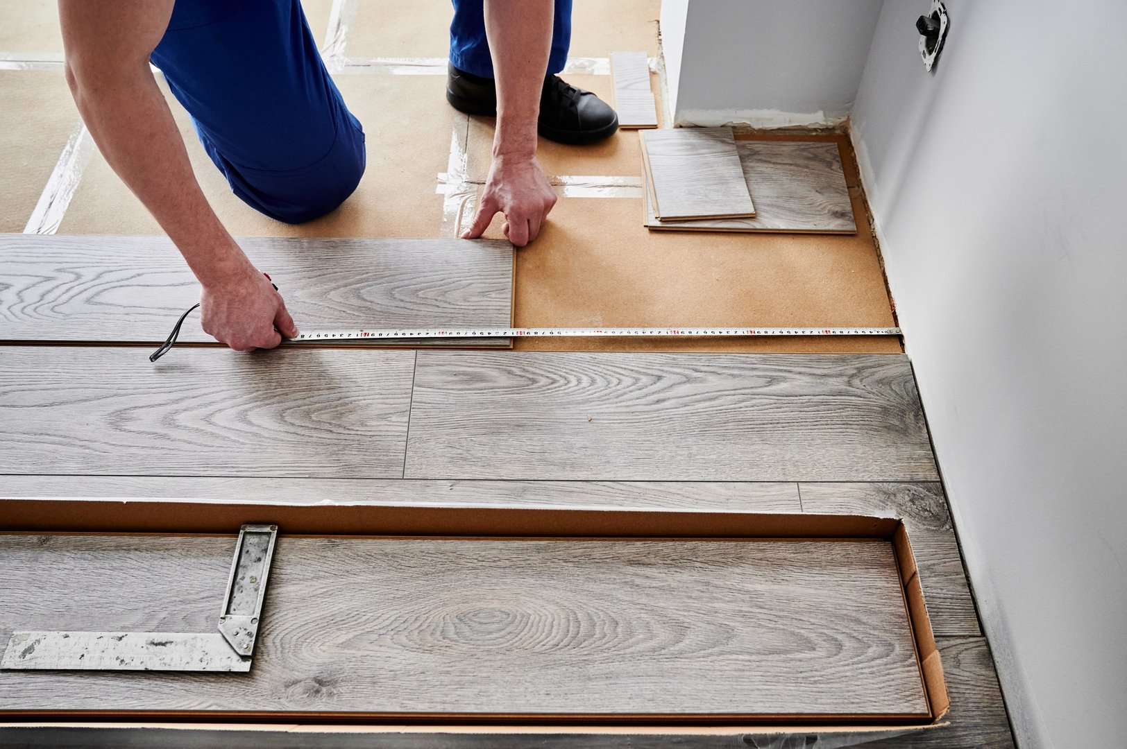 Male hands measuring distance from wall to laminate flooring plank.