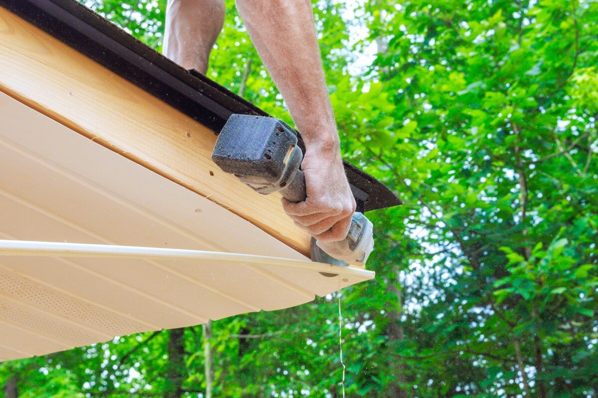 Cutting off existing vinyl soffit plastic panels on new house facade ceiling to a specific size