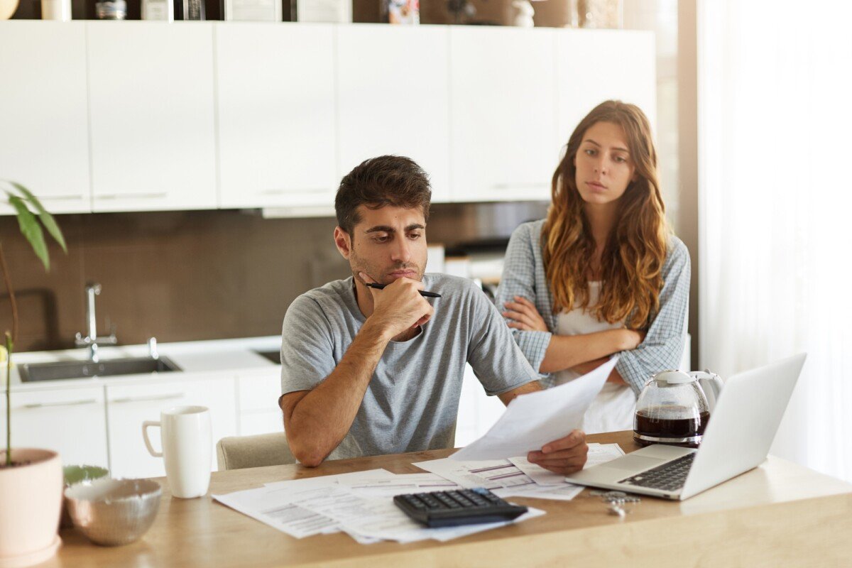 Frustrated young European couple facing financial crisis. Man with stubble sitting at kitchen table