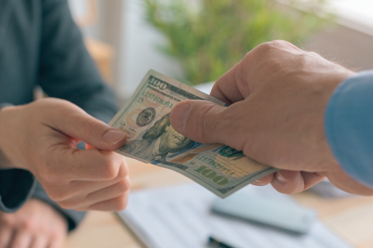 Hush money and corruption in business concept, close up of male hand giving hundred US dollar bill to female business person
