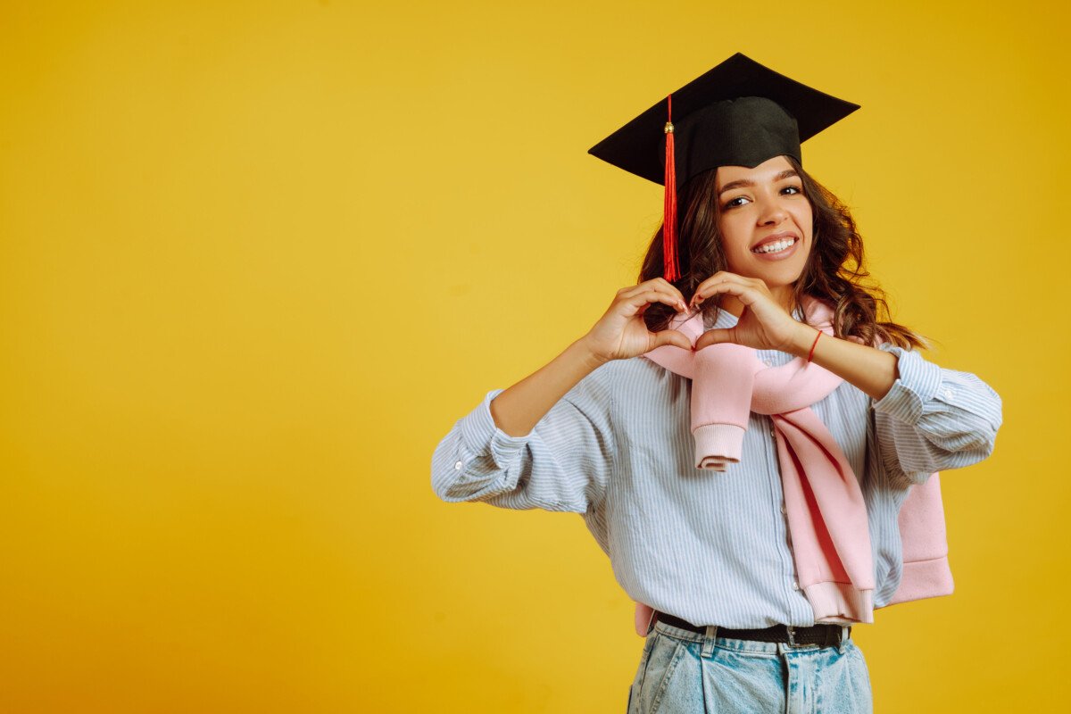 African American woman in a graduation hat on her head shows the heart symbol on the chest with his hands.