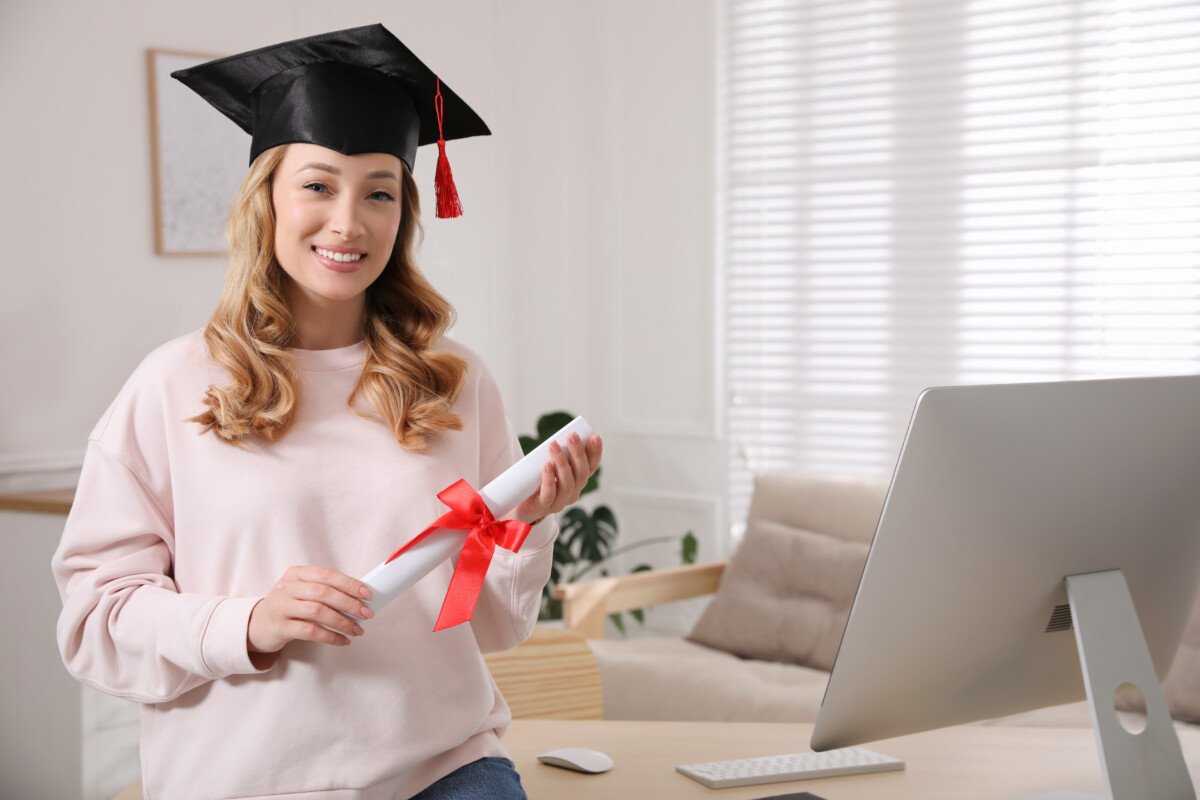 Happy student with graduation hat and diploma at workplace in office