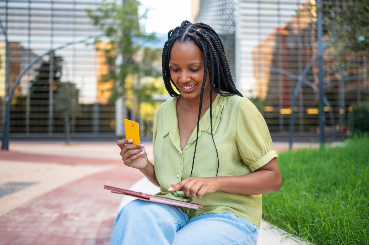 Young woman is using tablet and credit card for online shopping while sitting in a modern city park