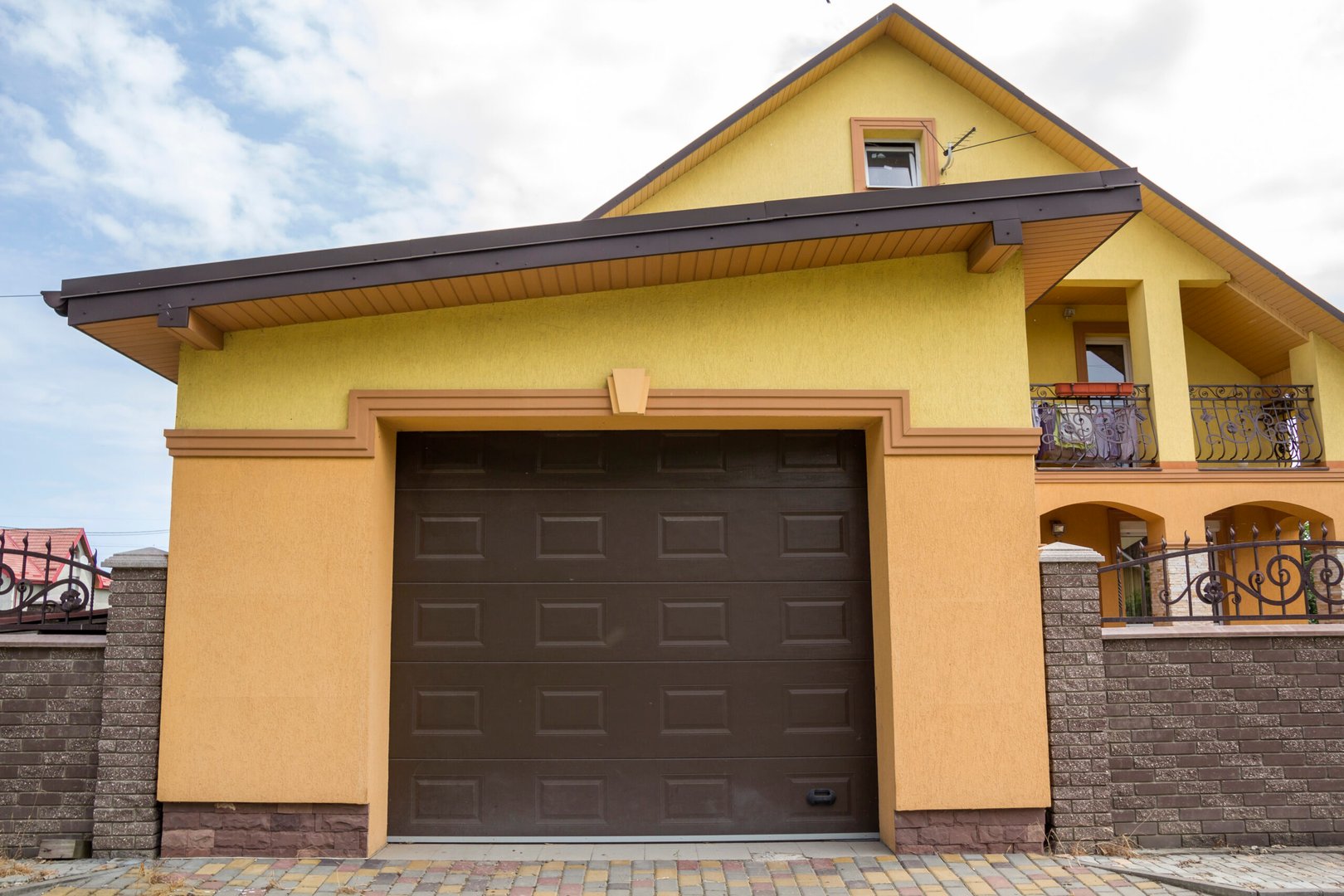 View from the clean paved street of detached garage with big automatic door, new residential cottage with balcony behind…