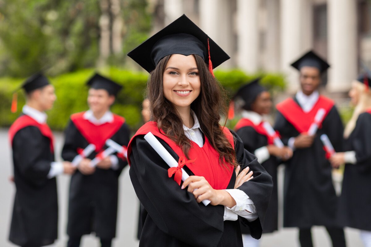 Positive pretty young lady student having graduation party, wearing graduation costume and holding diploma, happy female…