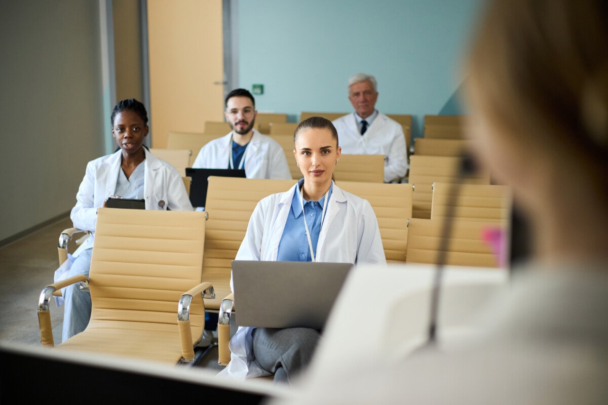 Group of diverse healthcare professionals attentively participating in a seminar in a modern conference room, engaging with…