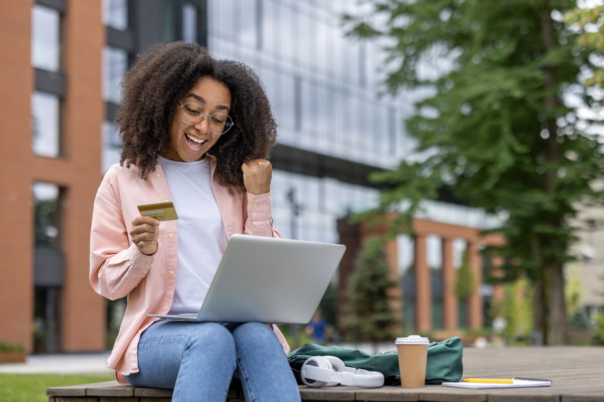 Excited african american woman making an online purchase using a laptop and credit card. Smiling student enjoying online…