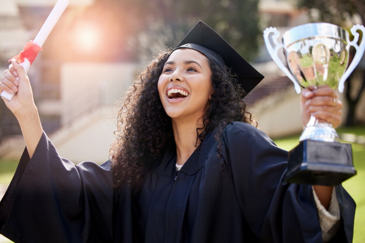 She came out tops. Shot of a young woman holding a trophy and cheering on graduation day