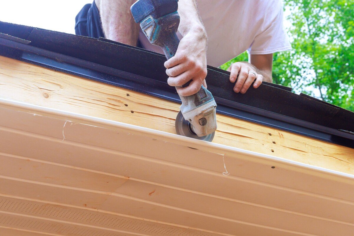 Employee cuts vinyl soffit plastic panels to required size on facade ceiling of a new residence
