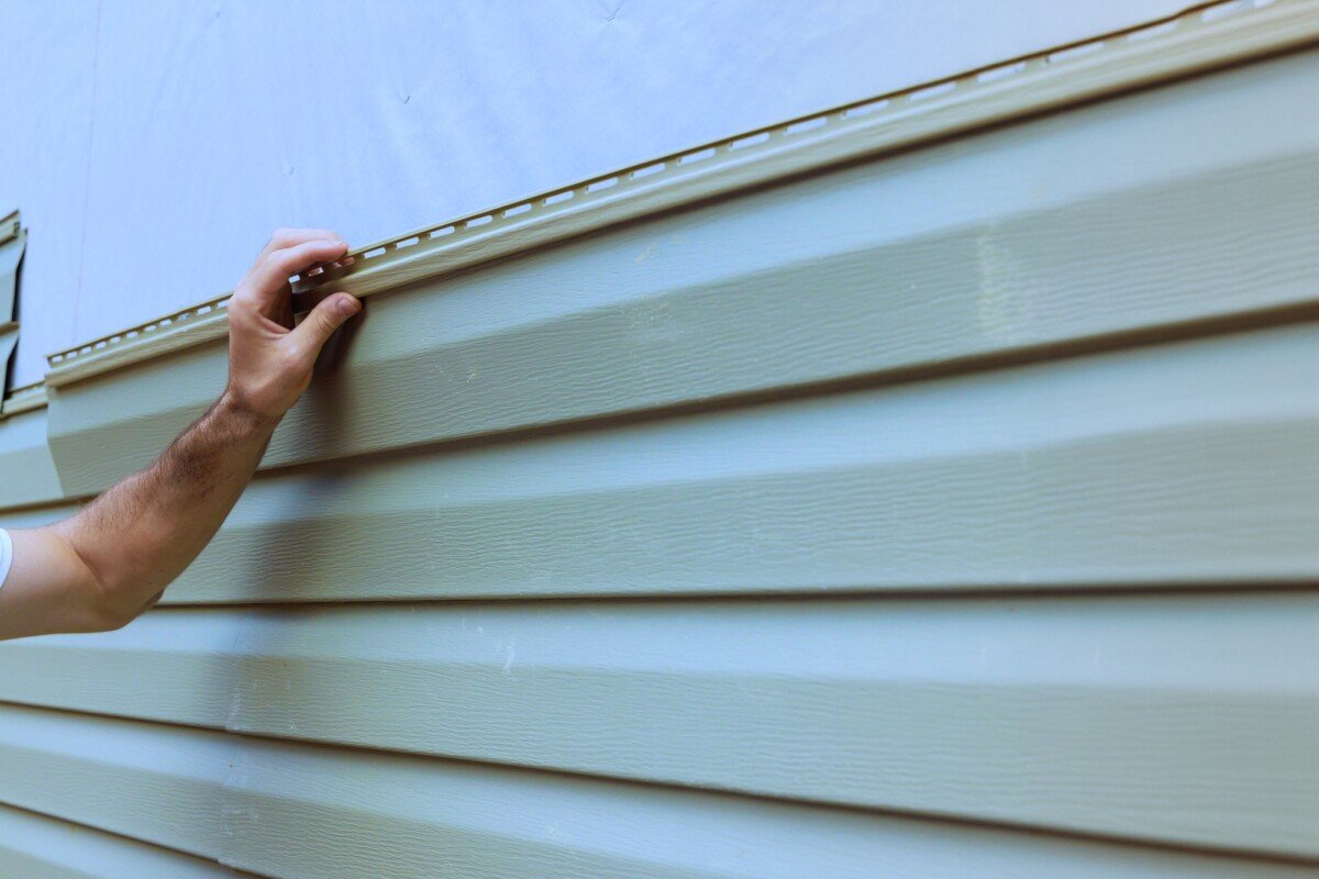 An experienced contractor installs vinyl siding plastic panels on facade wall of a new home