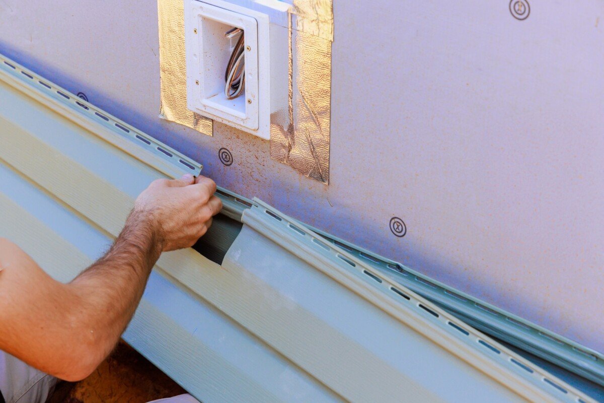 An employee installs panels of vinyl plastic siding on facade of a new house