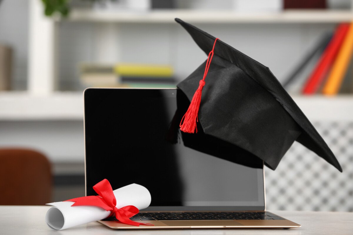 Graduation hat, student’s diploma and laptop on white table indoors