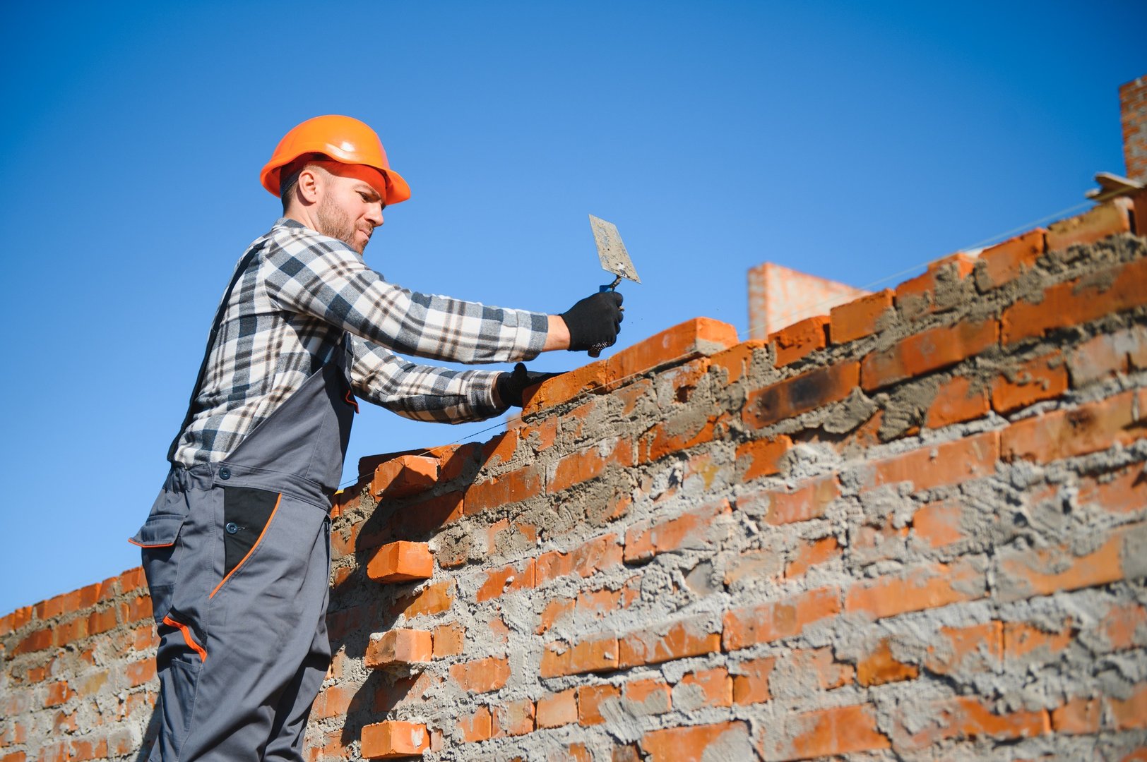 Bricklayer industrial worker installing brick masonry on exterior wall with trowel putty knife