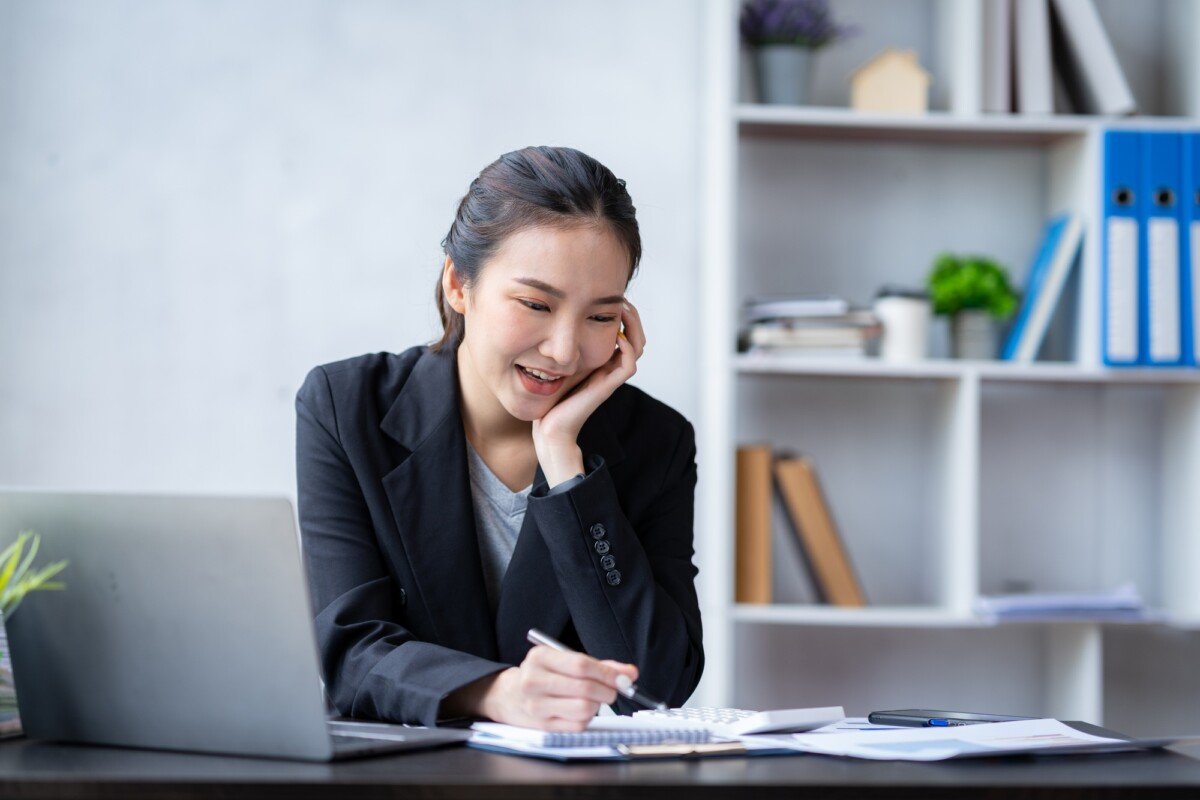 Portrait of an Asian businesswoman pressing a calculator, looking at a notebook, analyzing data, and