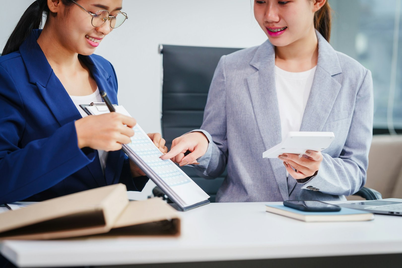 Two Asian businesswomen collaborate on stock market strategies and financial services, exchanging