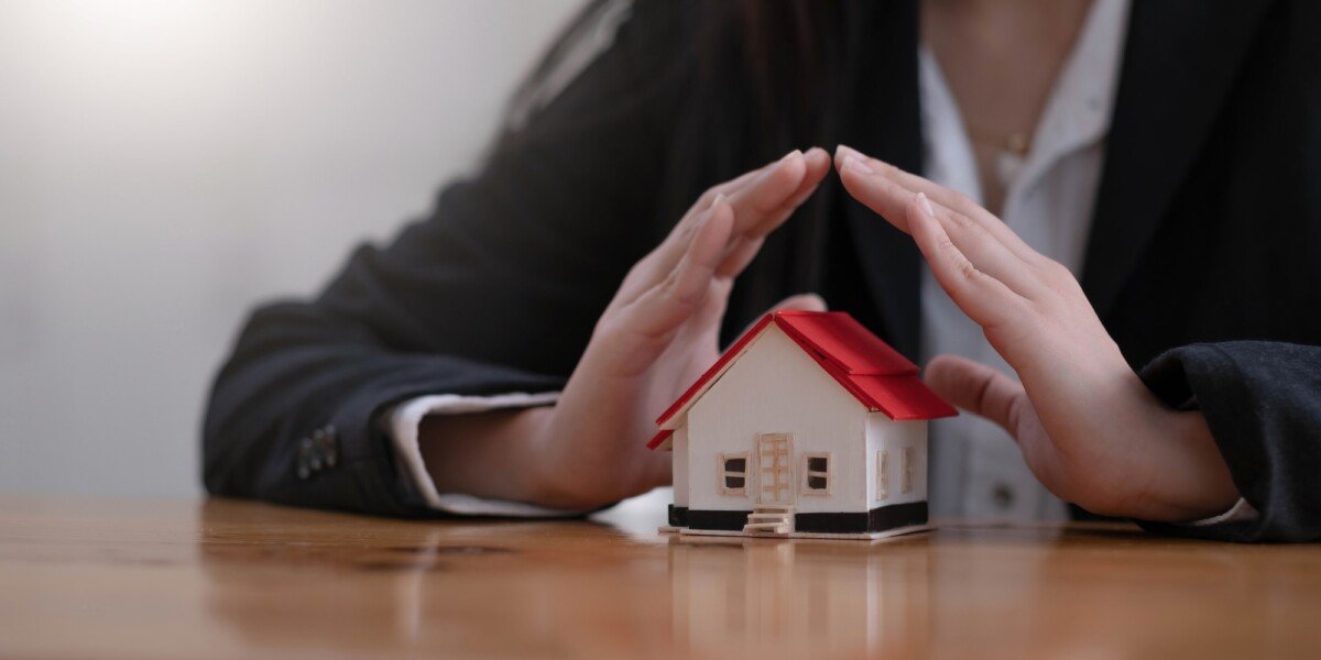 Protect your house concept. Small toy house covered by hands
