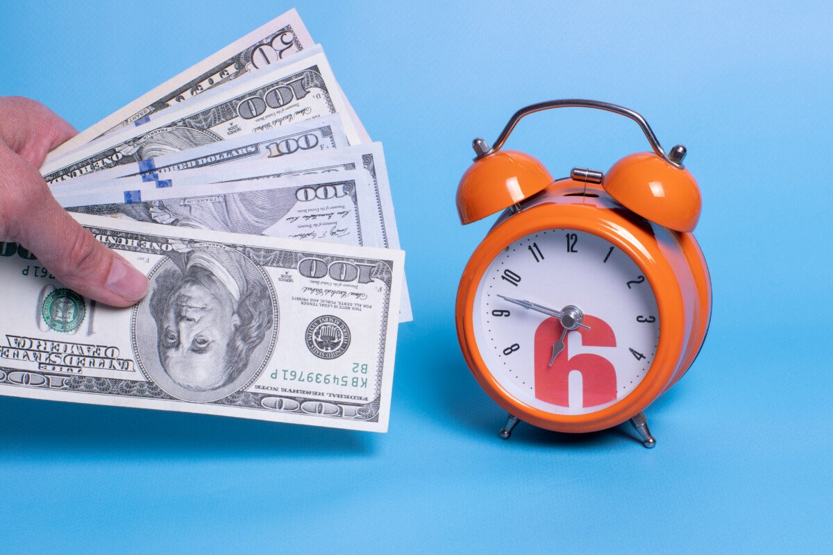 Hand holding money next to orange alarm clock. Concept for business planning, finance, savings, tax.