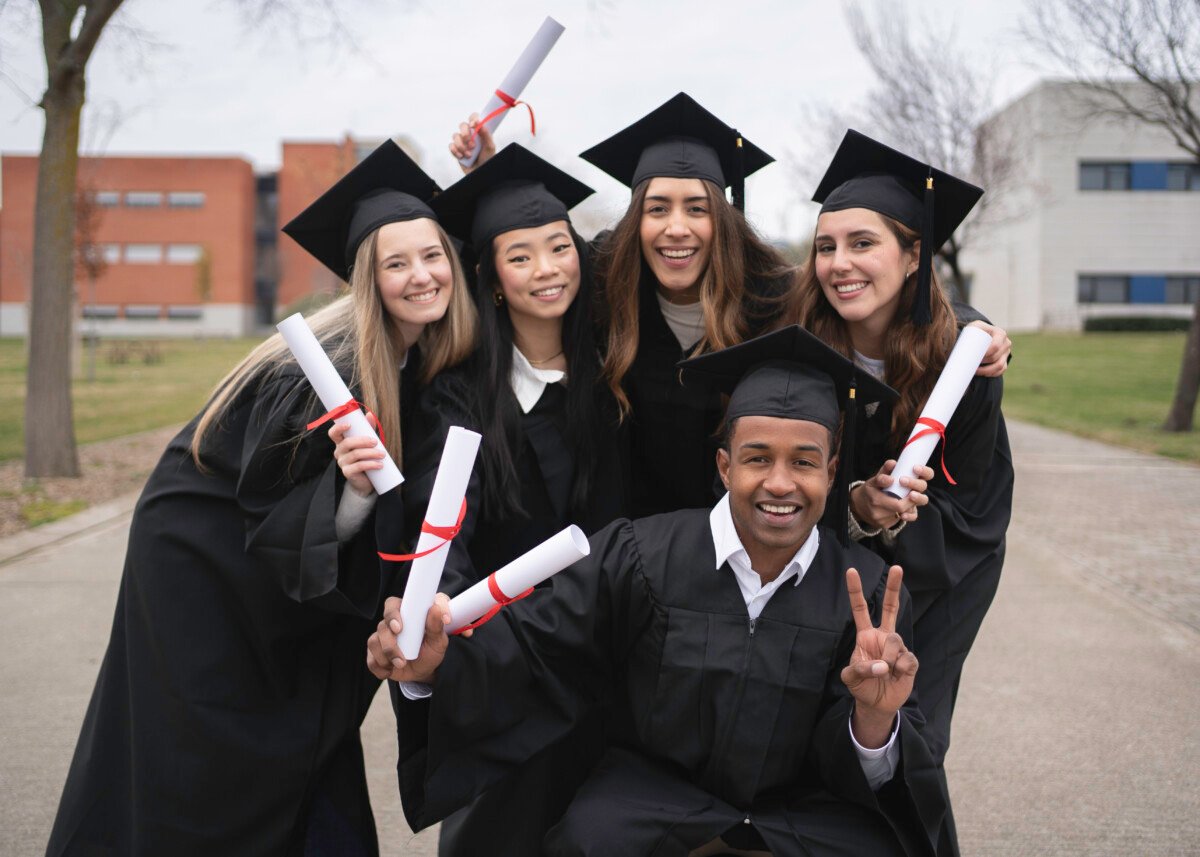 Group of cheerful multiethnic graduates wearing gowns and holding diplomas, celebrating their graduation