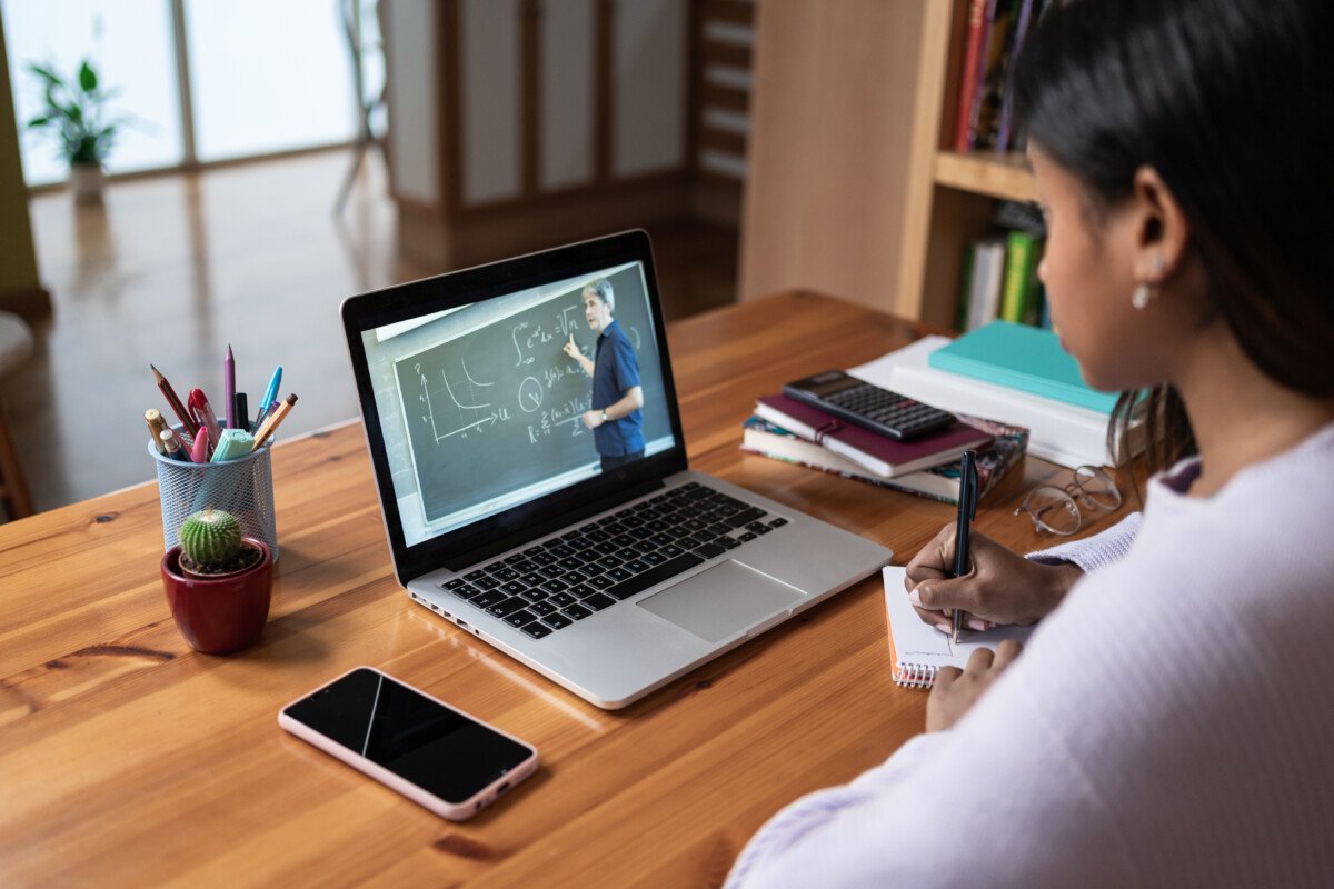Student taking notes watching online video class with Math Teacher from home