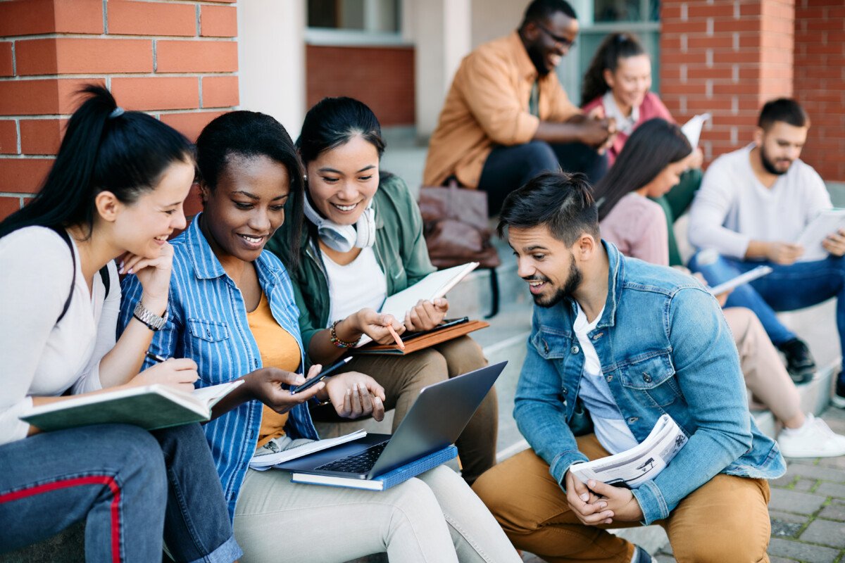 Multi-ethnic group of happy college friends surfing the net on laptop at campus.