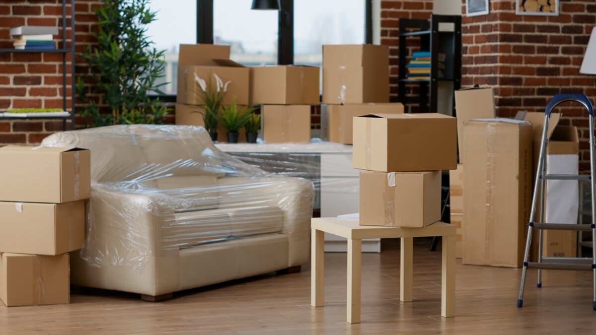 No people in empty living room apartment with carton boxes on stack, moving cardboard storage packaging in new household.…